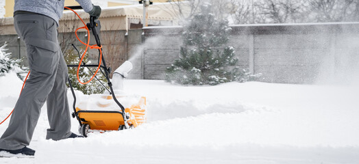 Man with machine removing snow in yard on winter day
