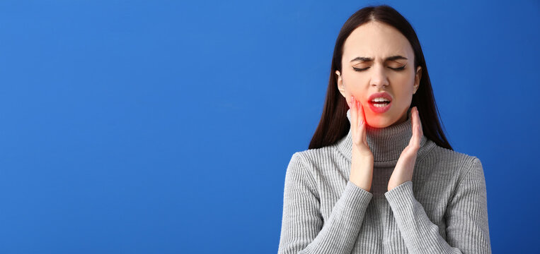 Young woman suffering from tooth ache on blue background with space for text