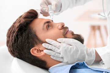 Obraz na płótnie Canvas Ophthalmologist putting drops in young man's eye at hospital, closeup
