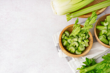 Wooden bowl with cut celery on light background