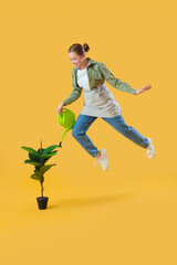 Obraz premium Female gardener with watering can and houseplant jumping on yellow background