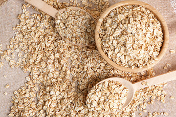 Bowl and spoons with raw oat flakes on fabric background, closeup