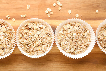 Wooden board with paper baking cups of raw oatmeal, closeup