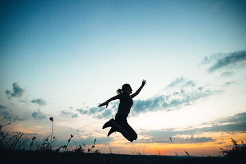 Fototapeta premium woman jumping with joy against sunset sky
