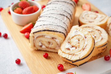 Cutting board with delicious sponge cake roll and fresh berries on light table