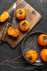 Wooden board and plate with fresh ripe persimmons on dark background