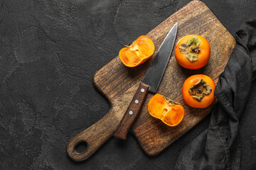 Wooden board with fresh ripe persimmons and knife on dark background