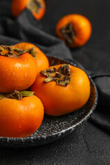 Plate with fresh ripe persimmons on dark background, closeup