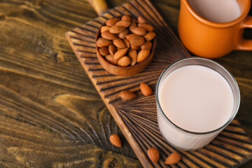 Cutting board with glass of healthy almond milk and nuts on wooden table