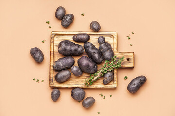 Wooden board with raw purple potatoes and thyme on color background