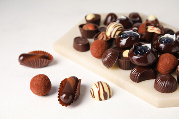 Board with chocolate candies on white background