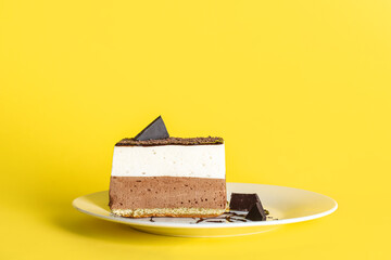 Plate with piece of birds milk cake and chocolate on yellow background
