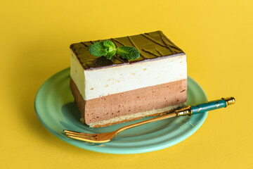 Plate with piece of birds milk cake, mint leaves and fork on yellow background