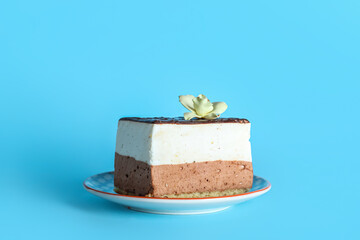 Plate with piece of birds milk cake and vanilla flower on blue background