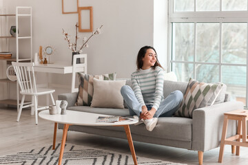 Young woman sitting on grey couch in living room - Powered by Adobe
