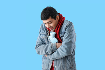 Young man warming with hot water bottle on blue background