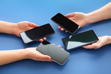 Female hands with mobile phones on blue background, closeup