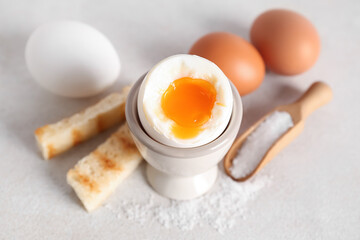Holder with soft boiled egg, toasted bread and scoop on white table