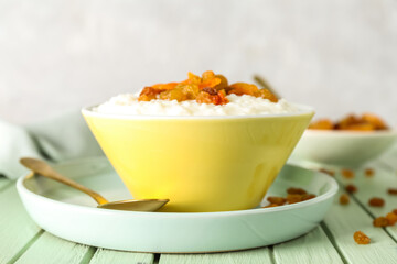 Bowl with delicious rice pudding, raisins, dried apricot and spoon on green wooden table