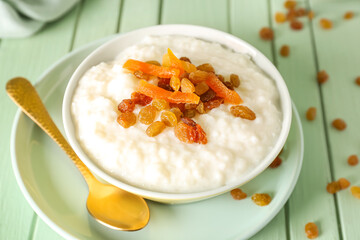 Bowl with delicious rice pudding, raisins, dried apricot and spoon on green wooden table