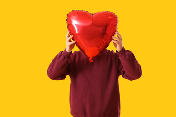 Young man with balloon for Valentine's Day on yellow background