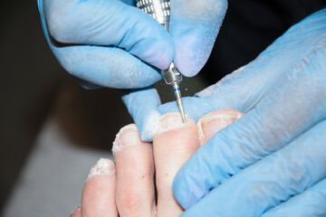 A master in a beauty salon makes a hardware pedicure to a client, soft focus 