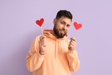 Young bearded man with paper hearts for Valentine's Day on lilac background