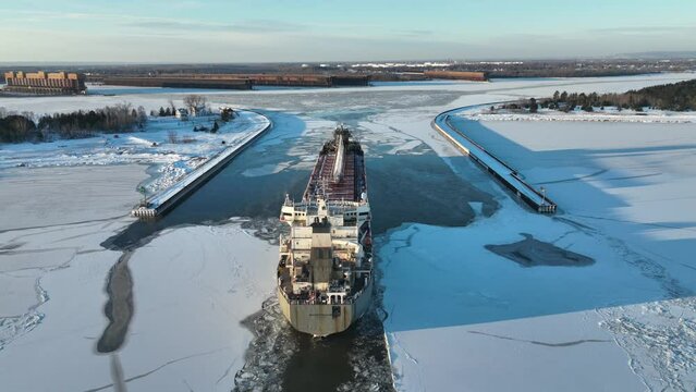 Old lake bulk cargo ship pushing through ice into harbor on the Great Lakes. Drone footage of self-unloading bulk carrier in winter.