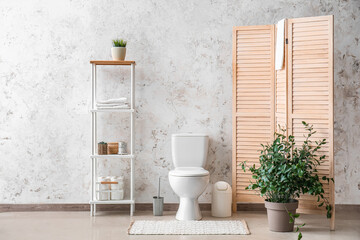 Interior of restroom with toilet bowl, shelving unit and folding screen