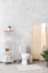 Interior of restroom with toilet bowl, shelving unit and folding screen