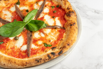Close up of pizza with anchovies, tomato sauce and mozzarella cheese on white marble table . High quality photo