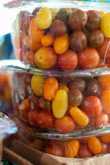 A stack of small clear plastic containers of raw organic cherry tomatoes on a grocery store shelf in a store for sale. The ripe Roma tomatoes are firm with thick shiny skin in a square package.  