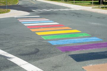 A multi-colored crosswalk painted on a paved road intersection with the colors of gay pride or...