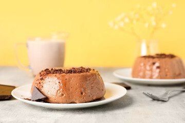 Plates with delicious pudding, chocolate and cup of milk on grey table near yellow wall