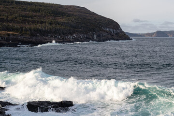 A seascape of a cloudy grey sky with a pink horizon that meets the grey ocean. There are a few...