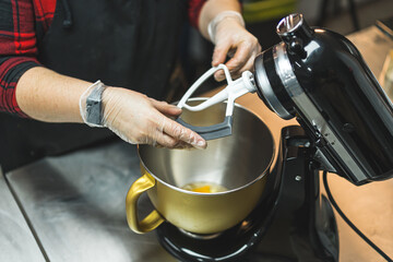 Baker wearing red plaid shirt, black apron and transparent gloves preparing black food mixer. High quality photo