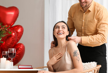 Young man putting necklace around his girlfriend's neck in kitchen on Valentine's Day