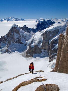 An alpinist climbs  the steep northwest face of Cerro Torre, with the peaks of Cerro Rincon and the glaciers of the SouthernPata