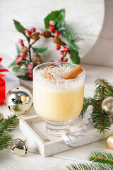 Glass of tasty eggnog cocktail, fir branches and Christmas decorations on light wooden table