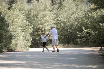 Obraz premium Back view of grandfather and grandson with hat walking on nature