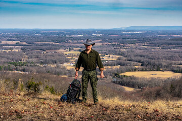 A man posing for a picture on a mountain looking from a cliff over the valley with a backpack filled with camping gear. At Keith Springs Mountain in Franklin County Tennessee USA.
