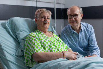 Elderly woman recovering from surgery with brother in hospital room. Sick lady being treated at gerontological clinic. Happy old man visiting hospitalized relative at sanatorium. - obrazy, fototapety, plakaty