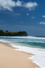 Fototapeta na wymiar Weißer tropischer Sandstrand mit strahlend blauen Meer und einer Felsen im Hintergrund, Indonesien, Bali