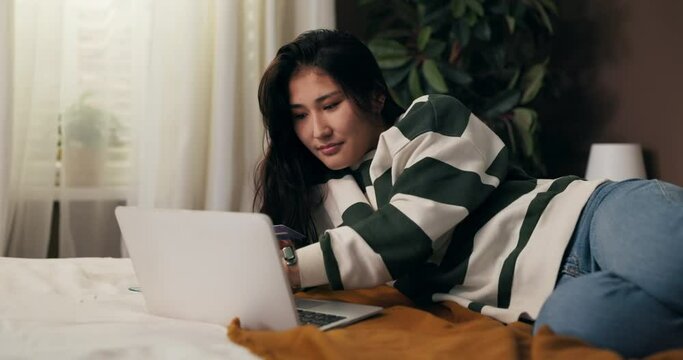 Beautiful woman lying on bed in bedroom buys trip to exotic countries, uses online travel agency, bookable hotel, pays for vacation with credit card.