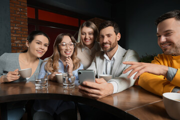 Handsome man showing something funny in smartphone to his friends in cafe