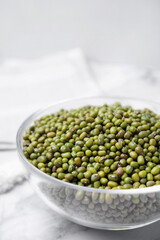 Glass bowl with green mung beans on white marble table, closeup