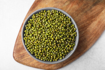 Bowl with green mung beans and wooden board on white table, top view