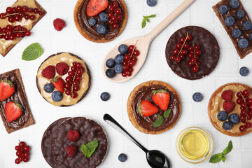 Fresh rye crispbreads, crunchy rice cakes and rusks with different toppings on white table, flat lay