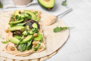 Tortilla with hummus and vegetables on white table, closeup. Space for text