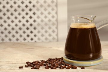 Glass turkish coffee pot with hot drink and beans on wooden table, space for text